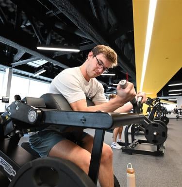 A man with short brown hair and glasses lifting weights.