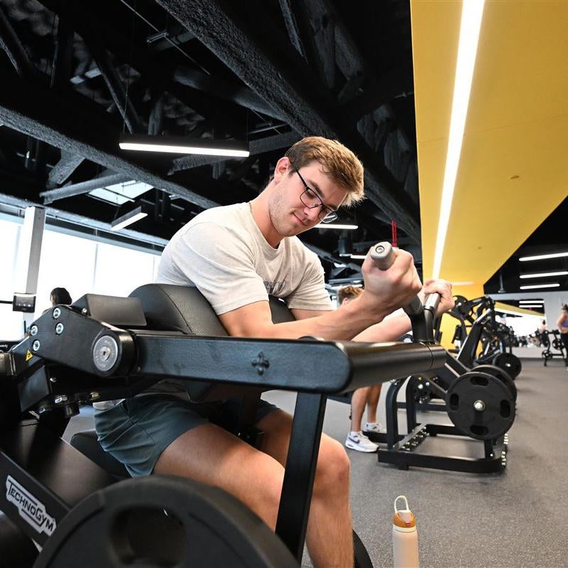 A man with short brown hair and glasses lifting weights.